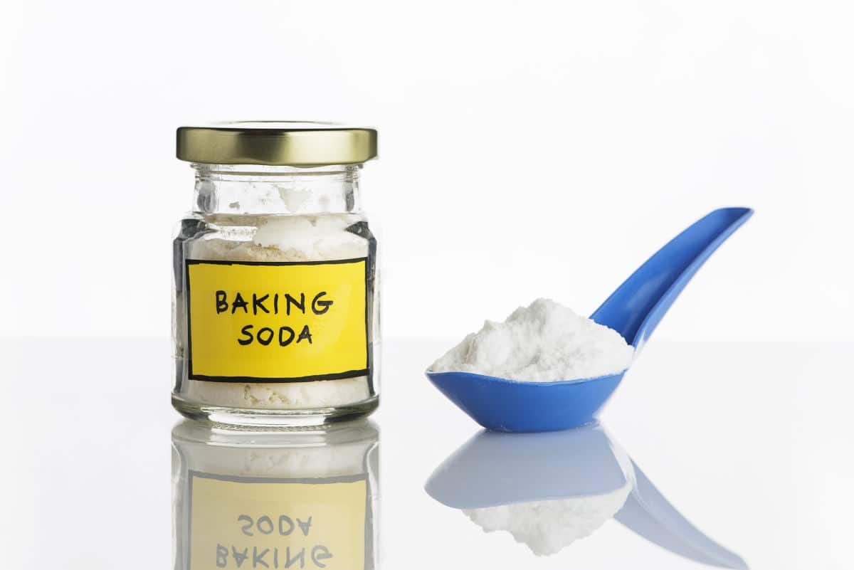 Jar of baking soda, yellow label and a blue spoon full of it