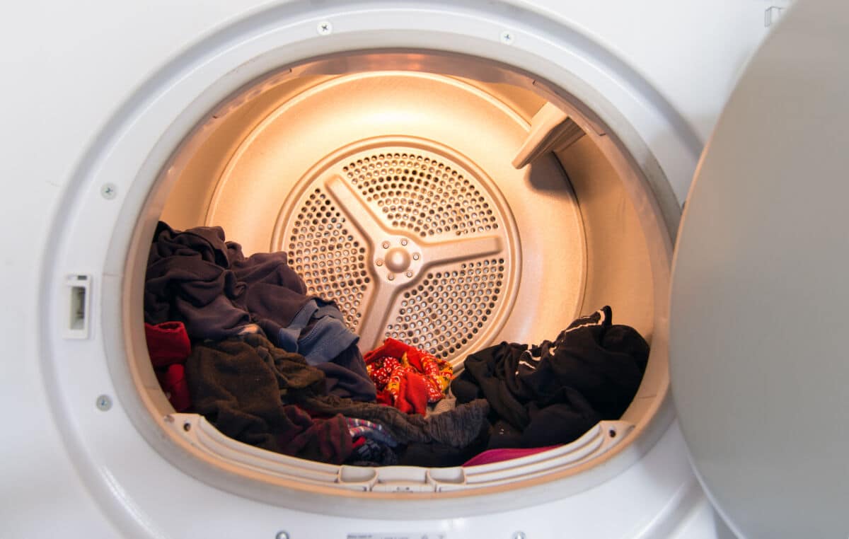 A clothes dryer, door open, half full of black and red clothes