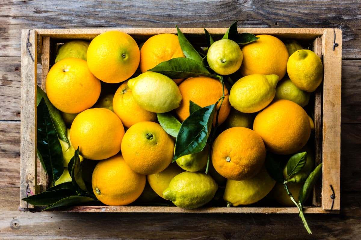 A wooden tray full of lemons and oranges, some with leaves still attached